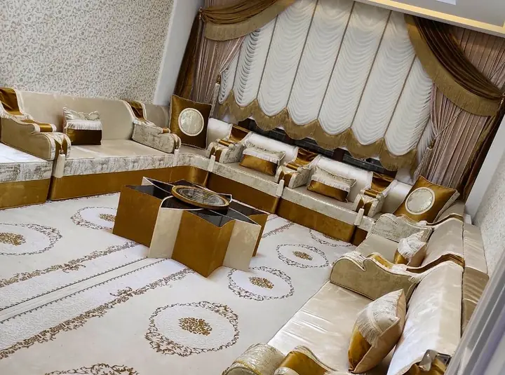 Ivory velvet majlis with gold trim around a star-shaped table set, a pale rug with gold medallions and swagged curtains
