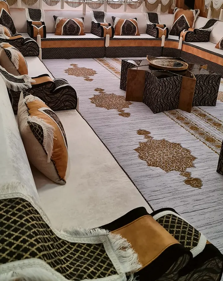 Ivory majlis seating along a curtained window wall, with caramel and black lattice cushions, a star-shaped table and a gold-medallion rug