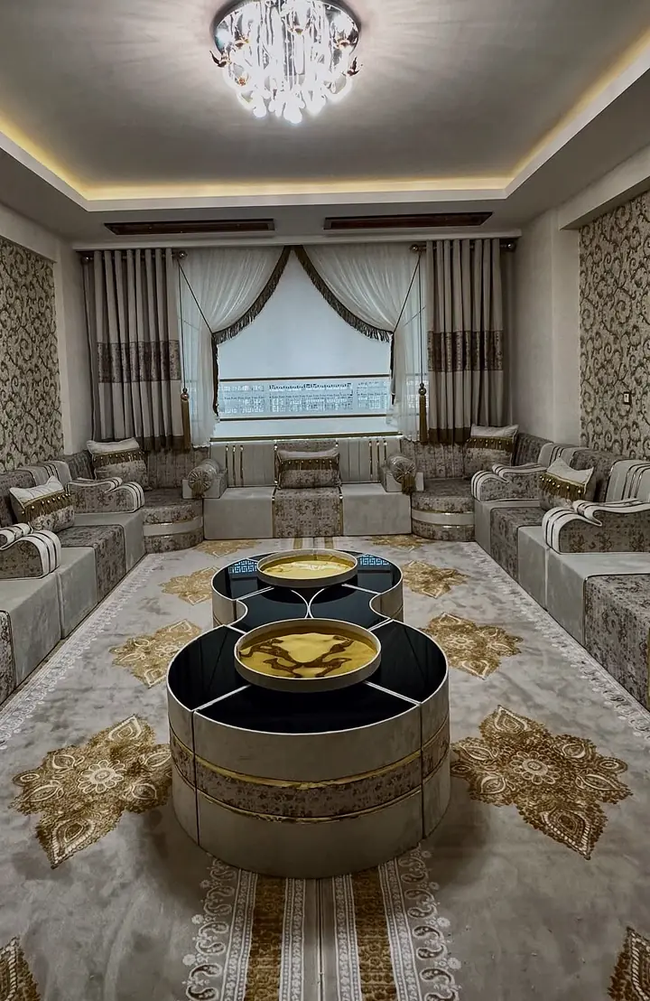 Ivory seating along both long walls under a crystal ceiling light, linked drum tables on a cream rug with gold paisley medallions