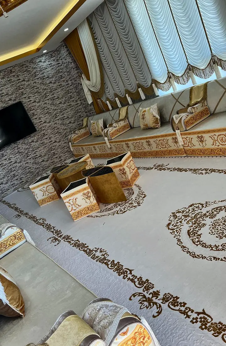 Ivory majlis with an orange baroque band along the base, a stone mosaic TV wall and an ivory rug with brown scrollwork