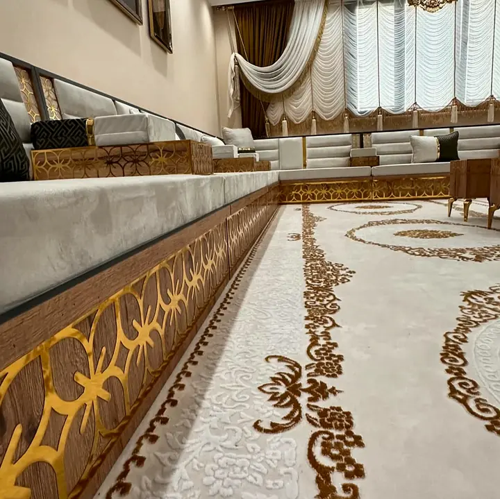 Close view along the walnut-tone plinth showing the gold quatrefoil lattice band under ivory seat cushions and a cream rug