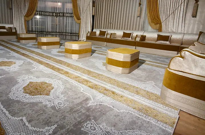 Ivory and mustard majlis along the walls of a large room, with banded cube ottomans on long cream and gold runner rugs