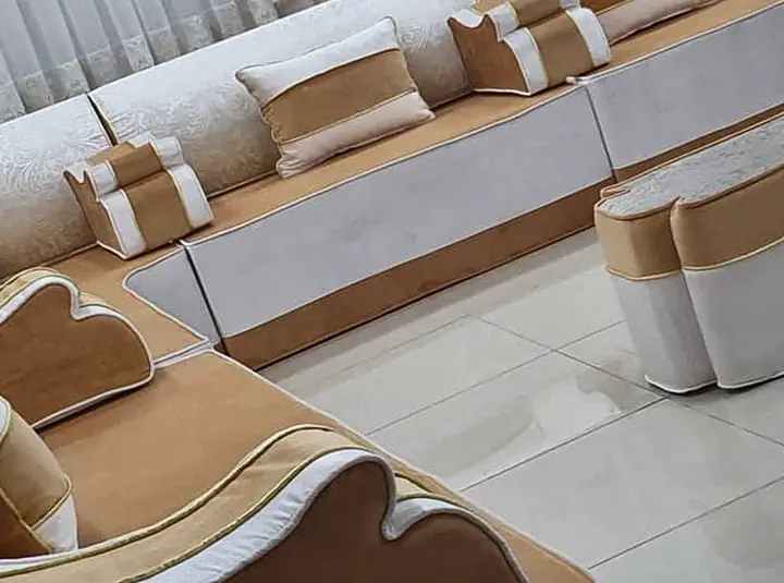 Ivory and mustard sofa-height majlis with scalloped armrests, piped edges and two tall matching ottomans on a white tile floor
