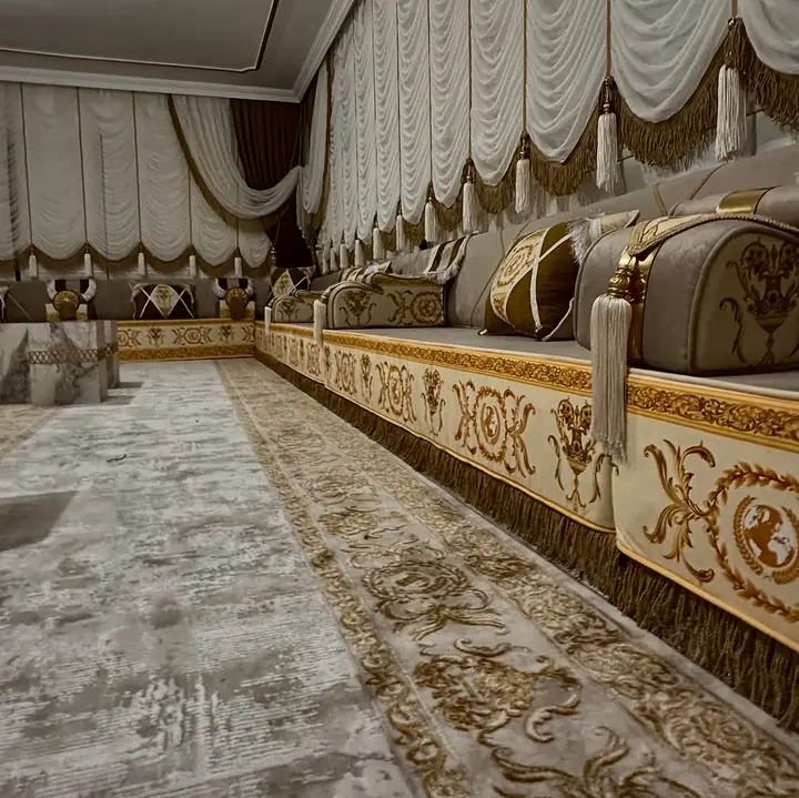 Close view of an ivory base printed with gold scrolls and medallions, finished with a deep gold fringe at the floor