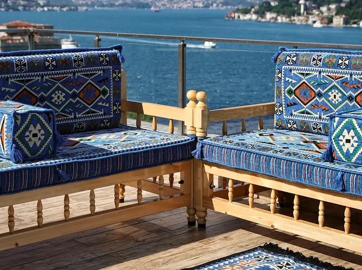 Corner where two blue village-pattern benches meet, the backrest pillows turning the angle above a rug