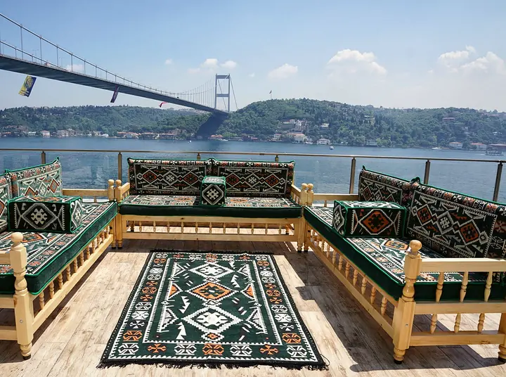 Green cushions with orange hooked diamonds on wooden benches arranged in a U around a matching flat-woven rug