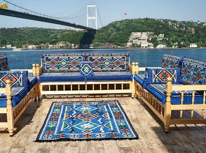 Three wooden benches with royal blue village-pattern cushions arranged in a U around a matching flat-woven rug