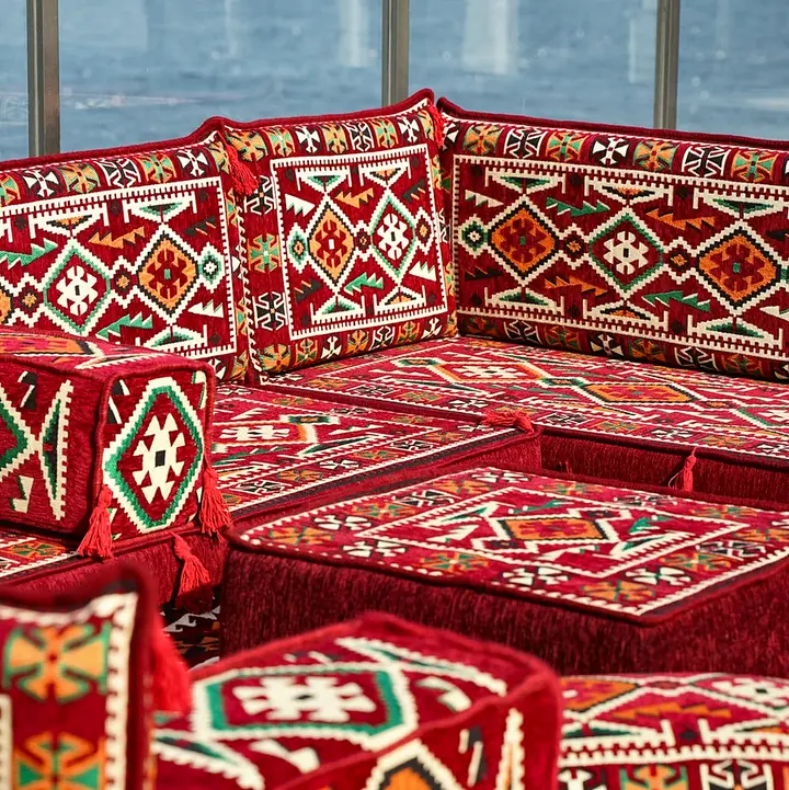 Close corner view of red kilim seats meeting at a right angle, with armrest bolsters beside the ottoman