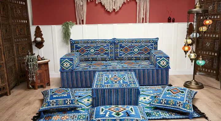 Blue kilim-pattern single floor sofa with a striped base, a blue ottoman and tasseled floor pillows below a macrame wall hanging