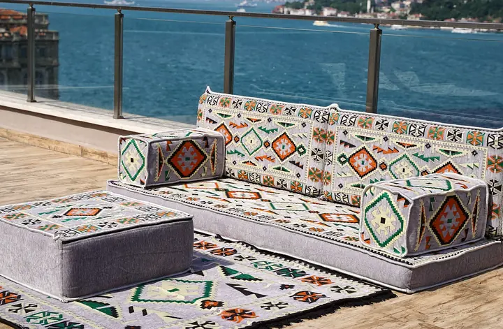 Light gray kilim seat with box armrests and a gray ottoman topped in kilim weave, resting on a matching rug, seen from a low side angle