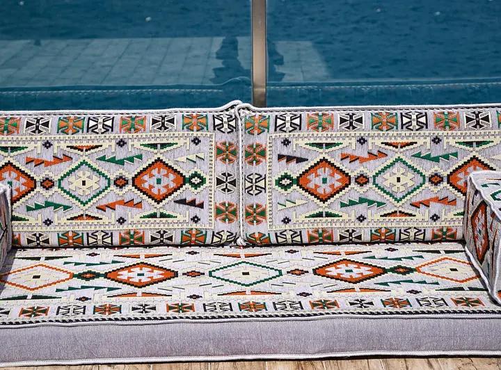 Front view of a light gray kilim single floor sofa with orange and green diamonds and square bolster armrests at both ends