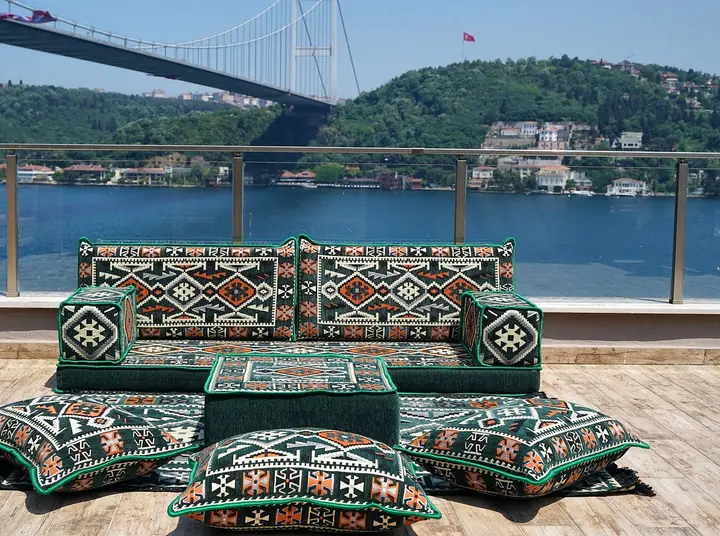 Dark green kilim seating with orange diamond accents, a green ottoman and floor pillows edged in green piping