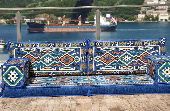 Front view of a royal blue kilim floor couch with two square bolster armrests and a deep blue fringed seat base
