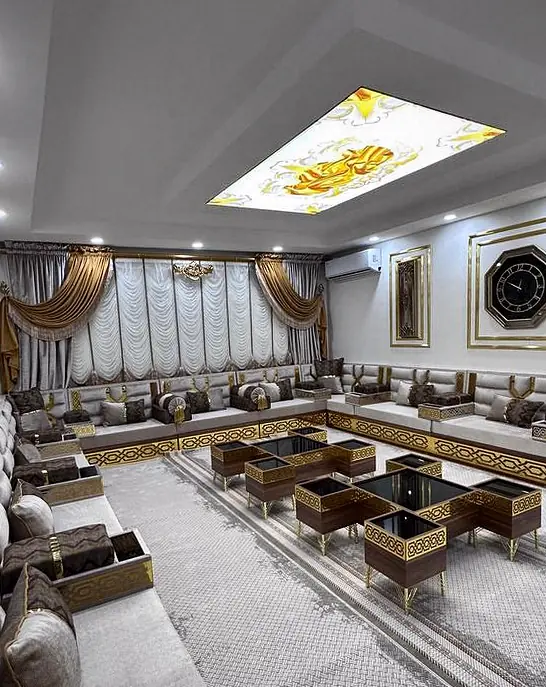 Angled view across a cream majlis room with a backlit ceiling panel over the seating and warm gold and brown accents