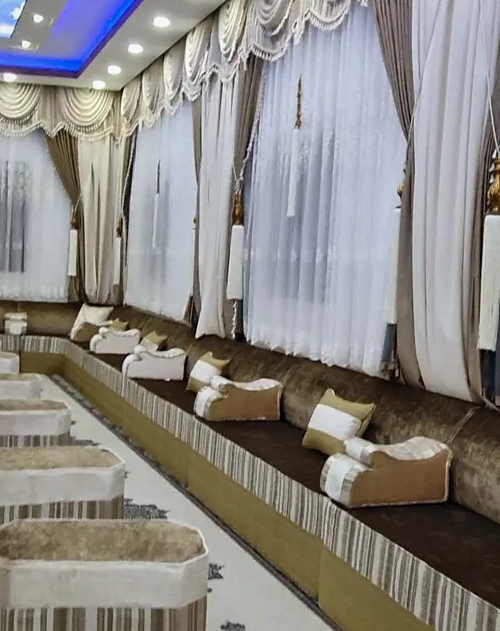 Very long hall with brown and ivory majlis seating on both walls, striped ottomans down the center and a white medallion runner