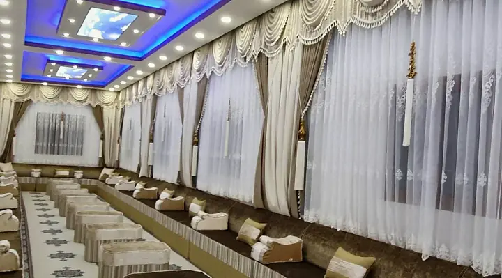 Long narrow hall with brown and cream seating along both walls, striped octagonal ottomans down the middle under a blue LED cove