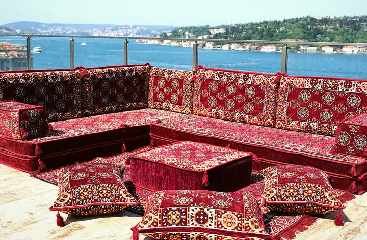 Maroon medallion-pattern L-shaped floor sofa with thick seat cushions, a matching ottoman and floor pillows on an open terrace