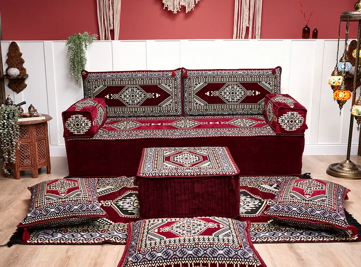 Maroon medallion single floor sofa set with a square ottoman, four floor pillows and a fringed rug beside glowing mosaic lamps