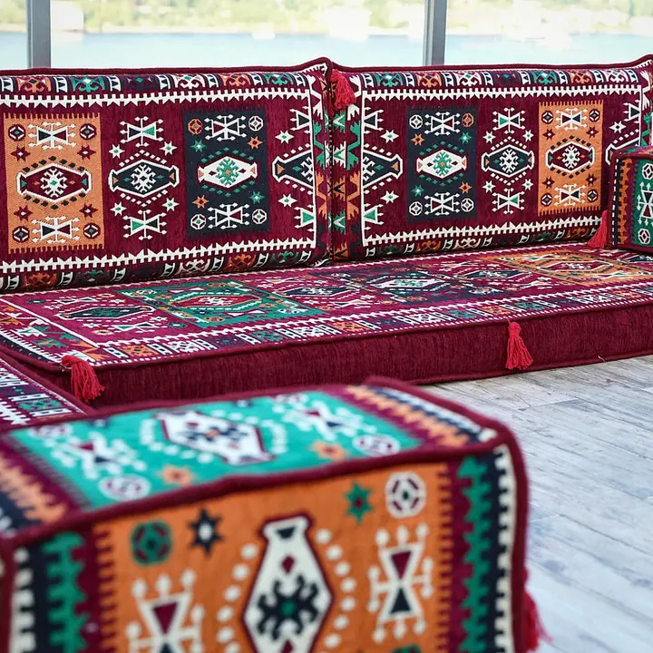Close view of a kilim-pattern armrest bolster in red, orange and teal, with the red seat softly blurred behind it