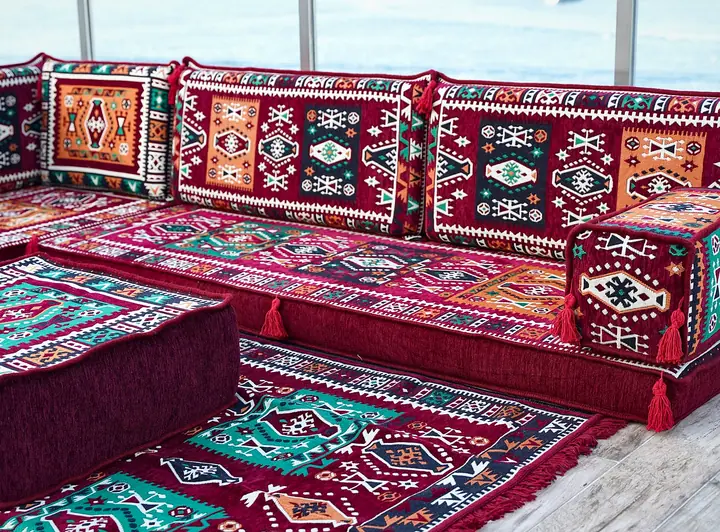 Red and orange kilim corner seating around a large plain velvet-look ottoman set on a kilim rug