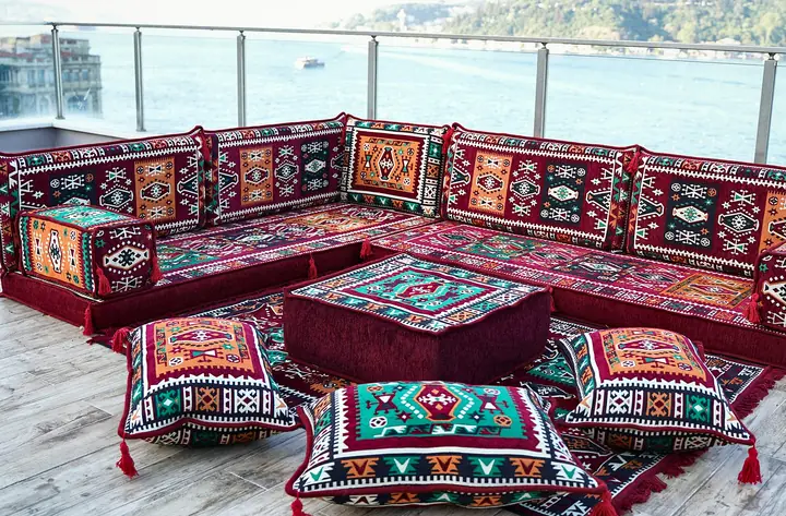 Corner floor seating in a red kilim weave with an ottoman and three floor pillows grouped in front of the seats