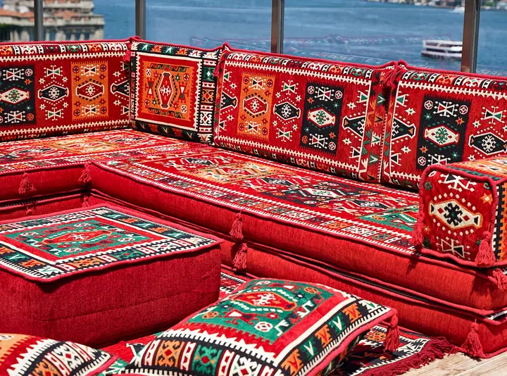 Thick red kilim seats meeting at a right-angle corner, with the ottoman and floor pillows placed close in front