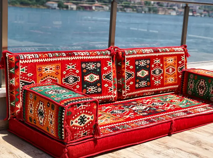 Angled view of a single red kilim seat with its two back cushions and a box armrest at each end, the front one filling the foreground