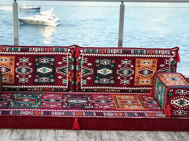 Front view of a single red kilim seat with teal and red armrest bolsters, resting on a gray wood floor