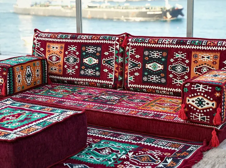 Close view of a red kilim seat with a teal armrest bolster sitting beside a plain velvet-look ottoman