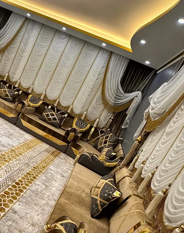 Brown seats with gold-edged quilted cushions line white drapes around dark nesting tables and a carpet with gold borders.