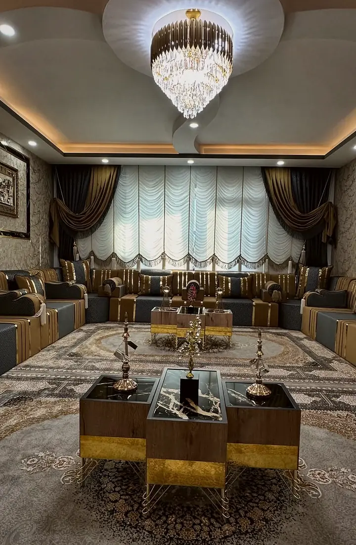 Mustard and charcoal majlis around a room with a crystal chandelier, a gray medallion rug and wood and black marble-look tables