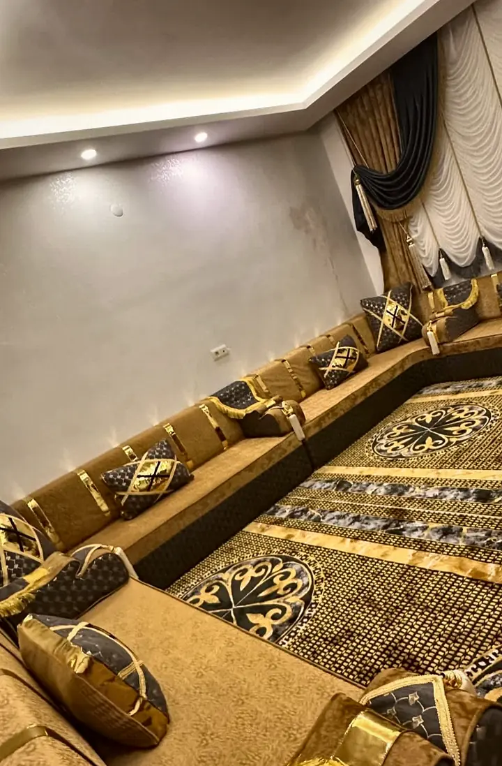 Long mustard gold velvet majlis on three walls with black quilted bands, gold-trimmed cushions, swagged curtains and a dark medallion rug