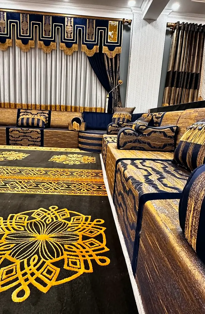 Gold mandala medallions on a black rug in front of a long navy and gold brocade majlis run with striped cushions and bolsters