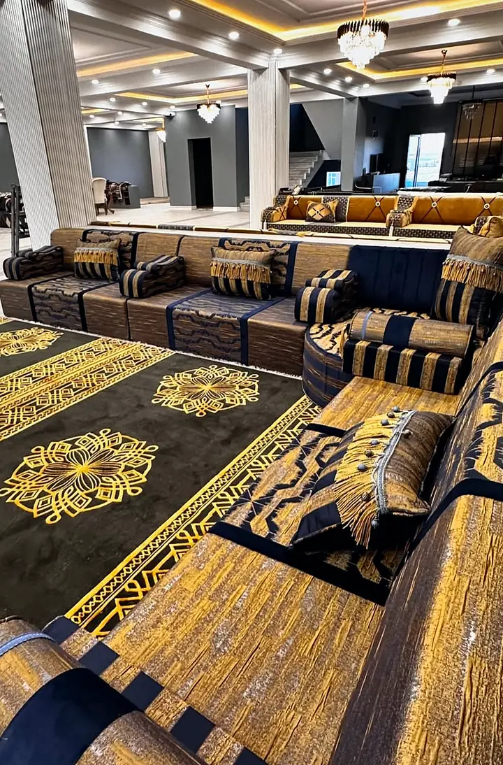 Navy and gold brocade majlis seen along one run, with striped navy bolsters and a black and gold rug, a second seating area beyond