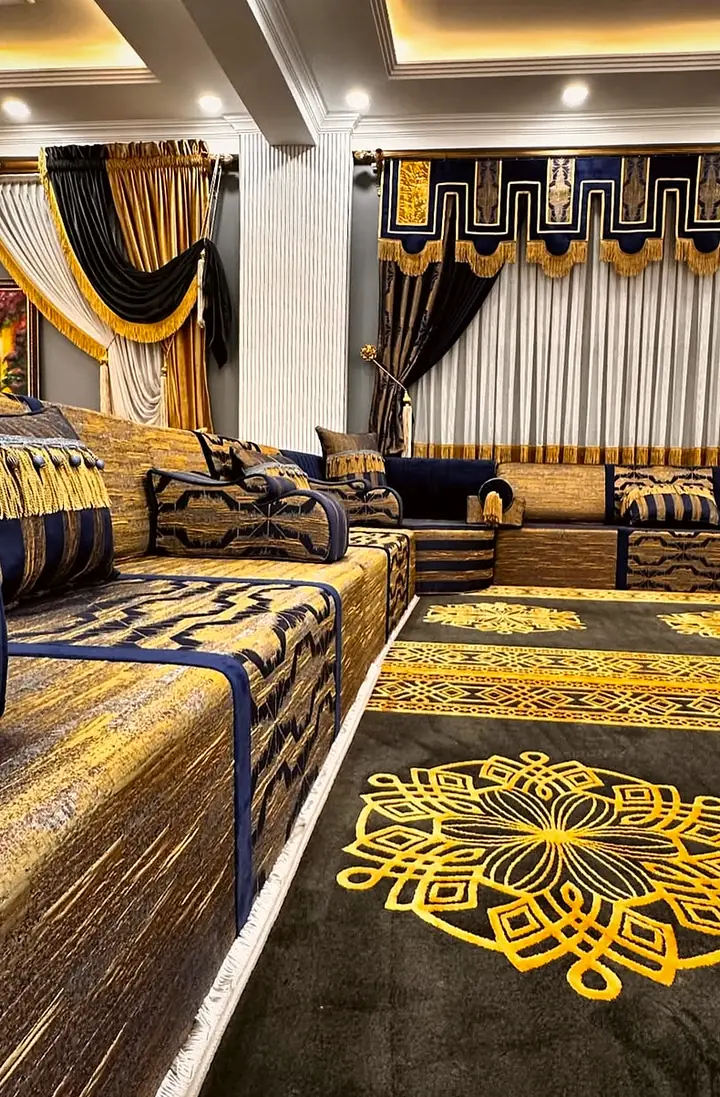 Navy and gold brocade seating with fringed striped bolsters along a black rug patterned with large gold knot medallions