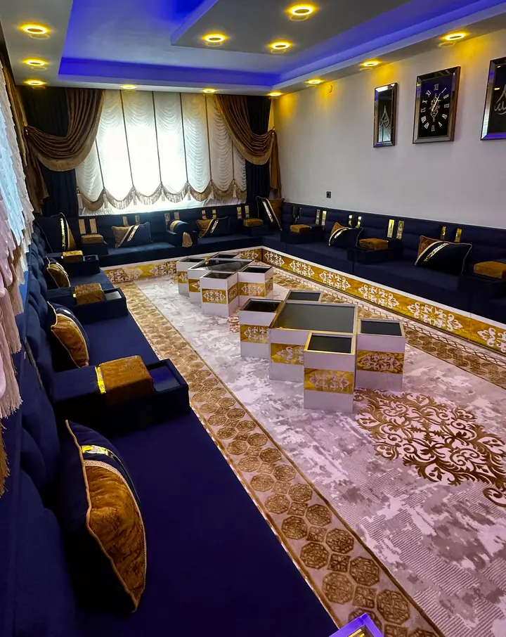 Navy seating along three walls under a ceiling washed in blue light, with gold pillows and cube tables on a cream and gold rug