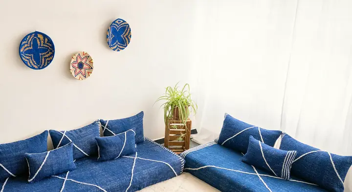 Two navy Moroccan-style floor couches with white line patterns along a wall, woven baskets above and plants on a cream rug