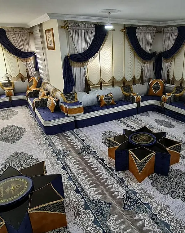 Navy velvet majlis around a large room with ivory front bands, mustard pillows, star-shaped tables, a patterned rug and cream swag curtains
