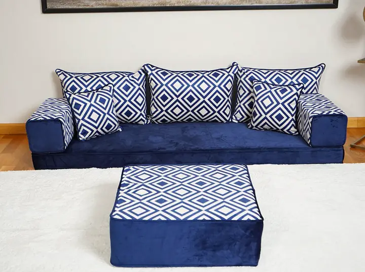 Navy velvet single floor sofa with blue and white geometric backrests and a matching square ottoman on a white rug