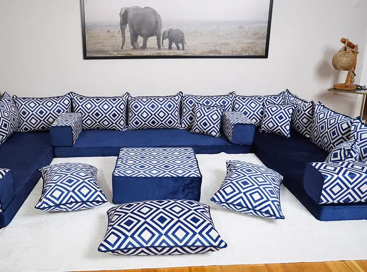 Navy velvet U-shaped floor sofa with white diamond-trellis backrest pillows, a matching ottoman and floor cushions on a pale rug