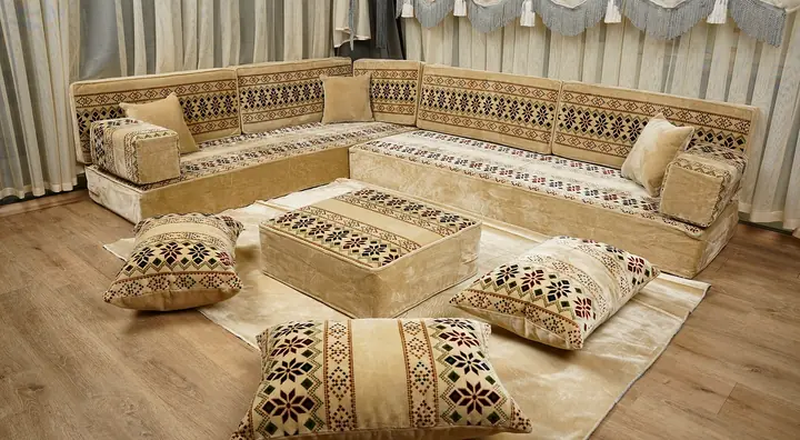 Embroidered-look red and black bands across cream cushions on an L-shaped floor sofa, with an ottoman and floor pillows