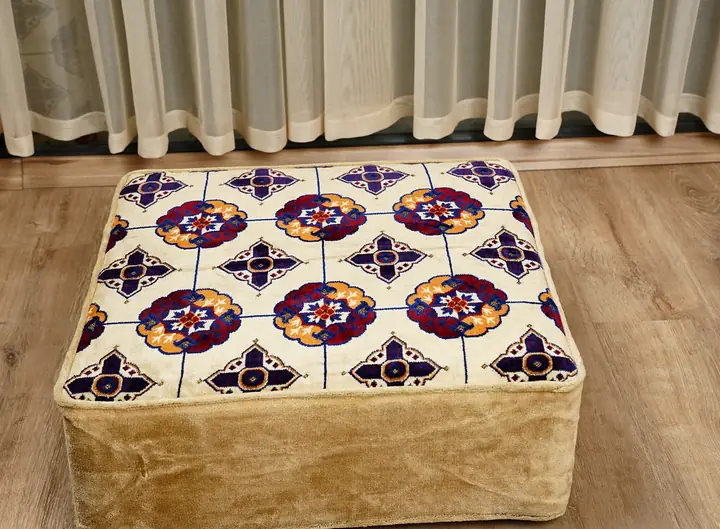 Square floor ottoman topped with plum and orange rosette medallions on cream, with soft beige sides