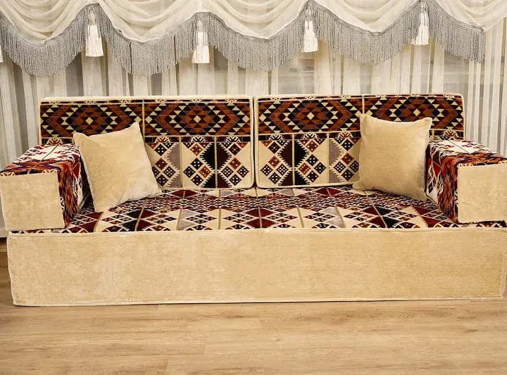 Front view of a single floor couch with red, brown and navy kilim diamond cushions on a cream base, bolsters at each end