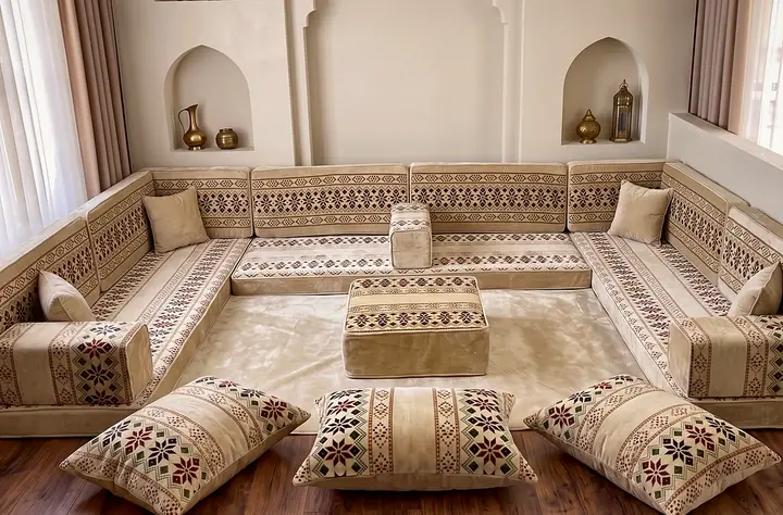 Cream floor majlis with red and brown cross-stitch-style bands on three walls, floor pillows below arched niches
