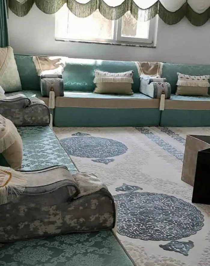 Pale teal damask majlis along three walls with cream bands, tasseled bolsters, scalloped valances and a star-shaped table on a cream rug