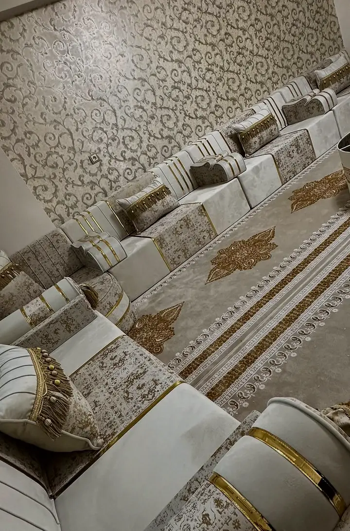 Ivory floor seats with gold bands and patterned cushions run along a floral wall beside round tables and a gold medallion carpet.