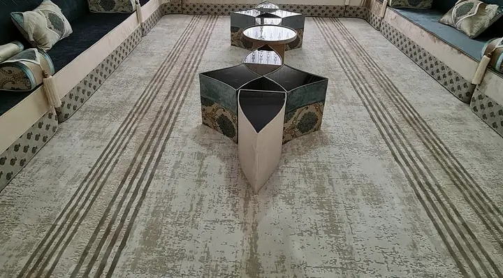 Petrol blue velvet U-shaped majlis with ivory piping, star-shaped tables on a gray striped rug and teal swag curtains
