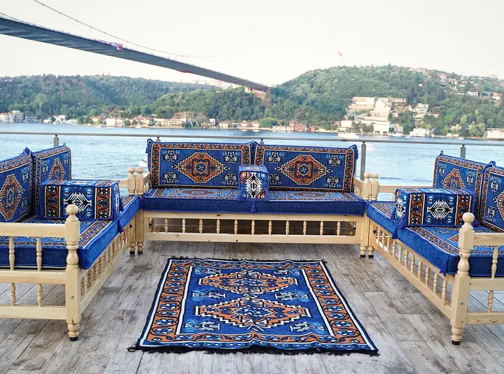 Three pine benches arranged around a patterned rug, with royal blue medallion cushions and a bridge visible through the window