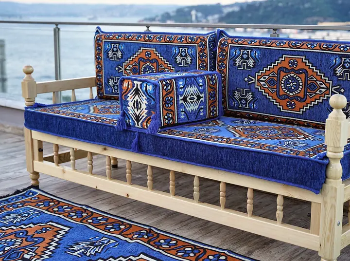 Single pine bench with turned spindles, royal blue and rust medallion cushions, a square bolster and a matching rug in front