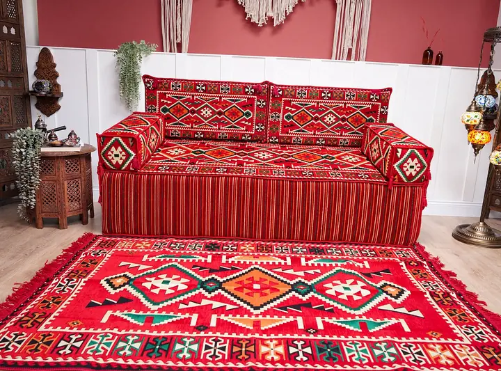 Red floor seating with white motifs behind a large matching fringed rug, a terracotta wall and a mosaic lamp